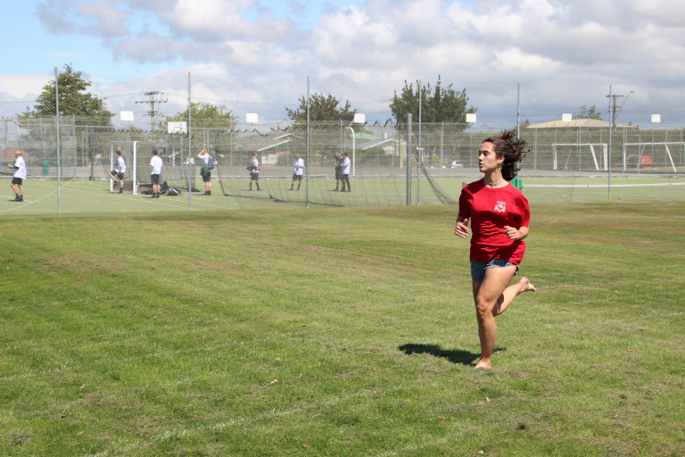 Student running barefooted on grass running track