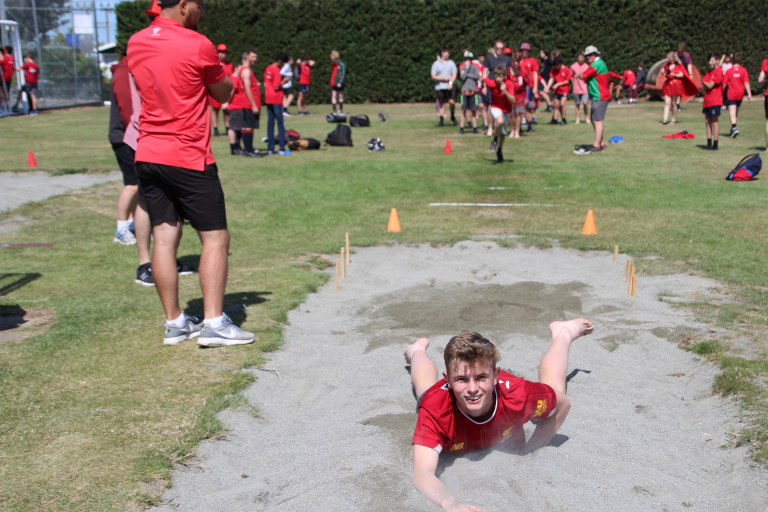 Student smiling, fallen over in long jump sand pit